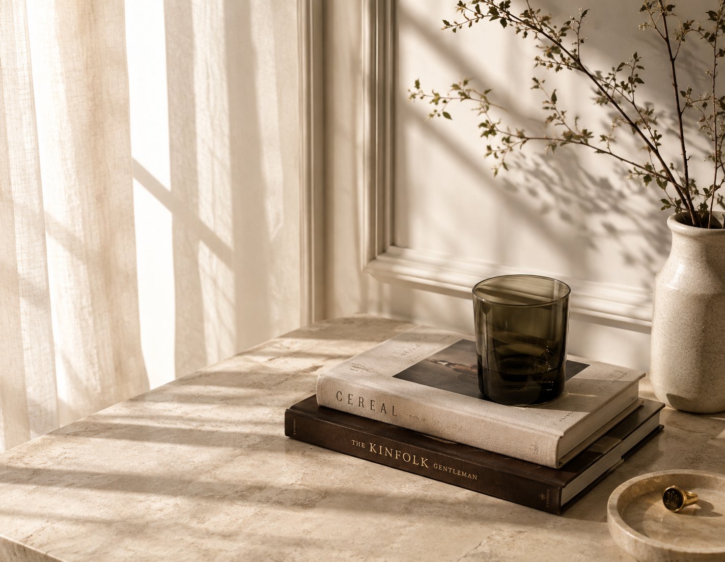 An ‘old money’ still life — soft linen light on marble, a stack of design books, a green glass, a signet ring in a dish